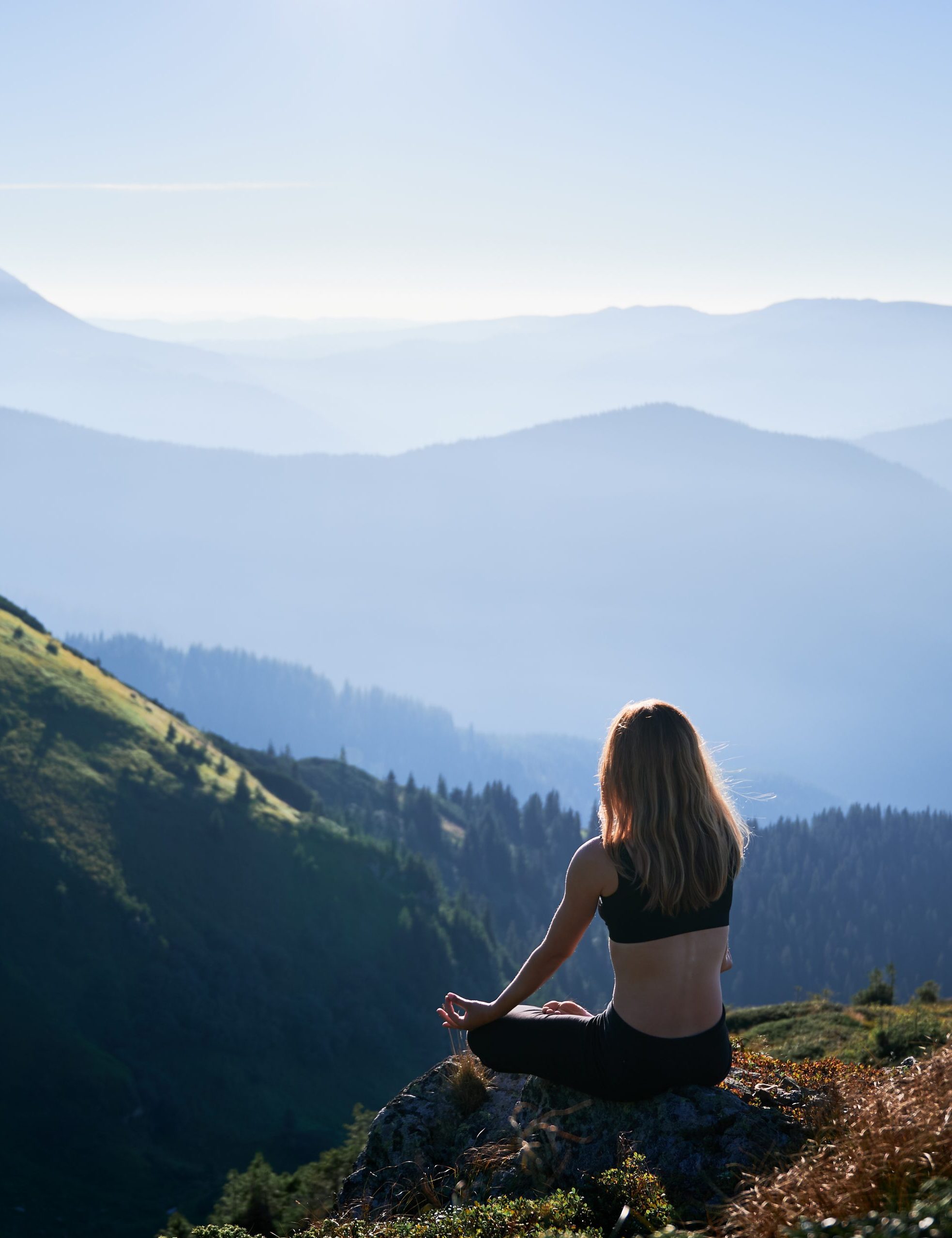 Brunette is meditating in Lotus pose in mountains.